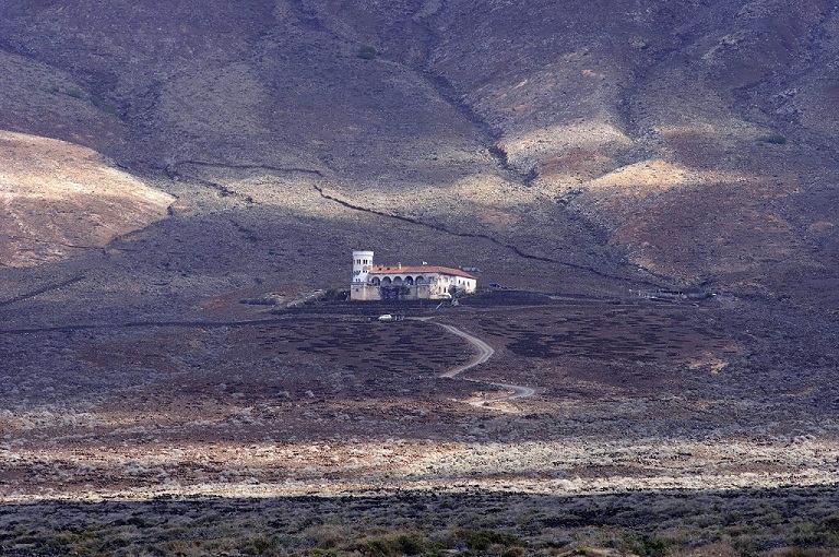 Kanaren buchen mit Fuerteventura in Erfurt bei REISEBÜRO Wache; im Bild: Die Villa Winter, ein weißes, großes Haus, im dunkelbraunen Vulkangebiet