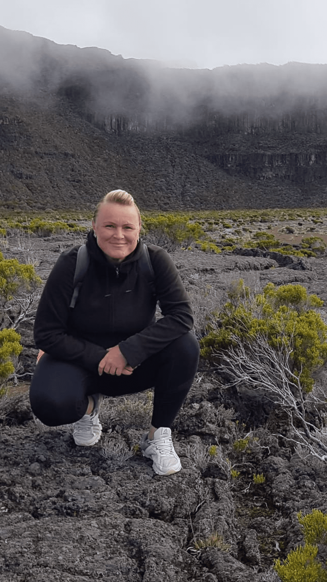 La Reunion Aktivurlaub Buchen Reisebuero Wache Erfurt La Réunion Urlaub buchen Aktivurlaub buchen beim REISEBÜRO Wache Erfurt; im Bild: eine blonde Frau, in Outdoor-Kleidung hockt auf einem erkalteten Lavafeld zwischen grünen Pflanzen, im Hintergrund Berge in Rauchwolken