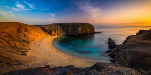 Urlaub Kanaren buchen, zum Beispiel Lanzarote, bei REISEBÜRO Wache Erfurt; im Bild: Sonnenuntergang am Strand Papagayo, eine Bucht, umrahmt von Felsen, davor blaues Wasser