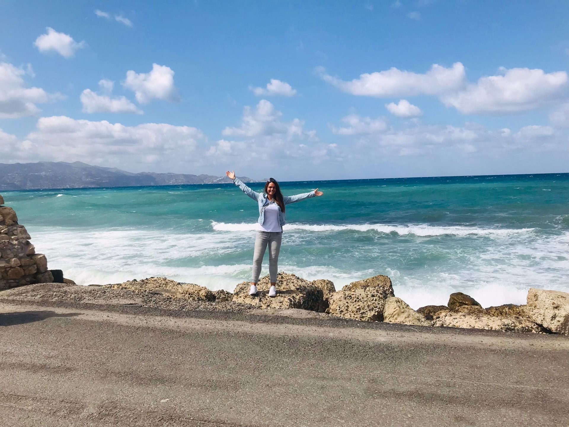 Reiseberaterin Sabrina Müller von REISEBÜRO Wache, Erfurt, auf Felsen vor tosendem, türkisfarbenem Meer auf Kreta, Griechenland, im Hintergrund Berge