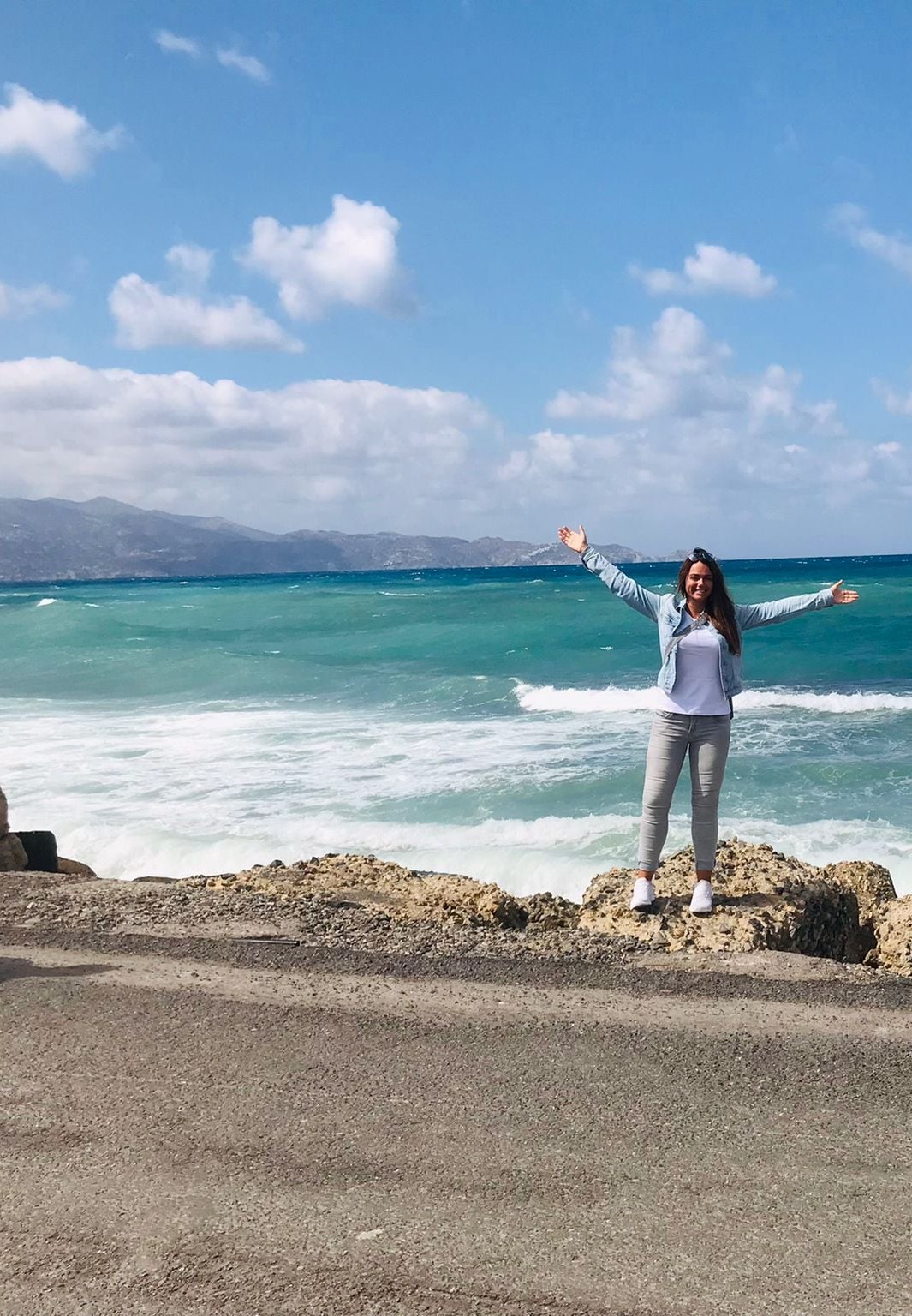 Sabrina Müller, Reiseberaterin bei REISEBÜRO Wache, Erfurt, auf Felsen vor tosendem türkisfarbenem Meer, im Hintergrund Berge