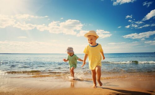 Aegypten Urlaub Erfurt Reisebuero Wache Ägypten Urlaub 2024 buchen in Erfurt bei REISEBÜRO Wache; im Bild: zwei kleine Kinder mit Sonnenhüten und T-Shirts am Strand, dahinter das Meer, über ihnen blauer Himmel mit Wölkchen