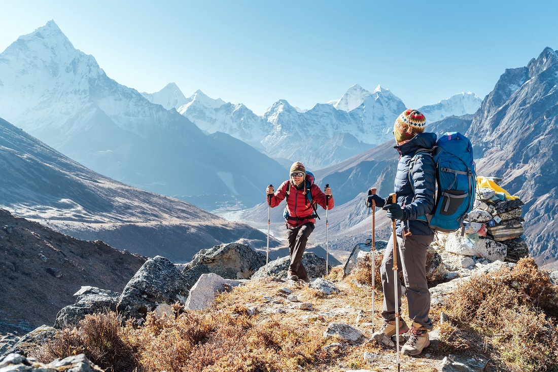 Bucket List Reise Trekking in Nepal, buchen beim REISEBÜRO Wache Erfurt; im Bild: Ein Mann und eine Frau mit Mützen und Jacken und Trekking-Stöcken auf einem Berg, im Hintergrund Berge des Himalayas