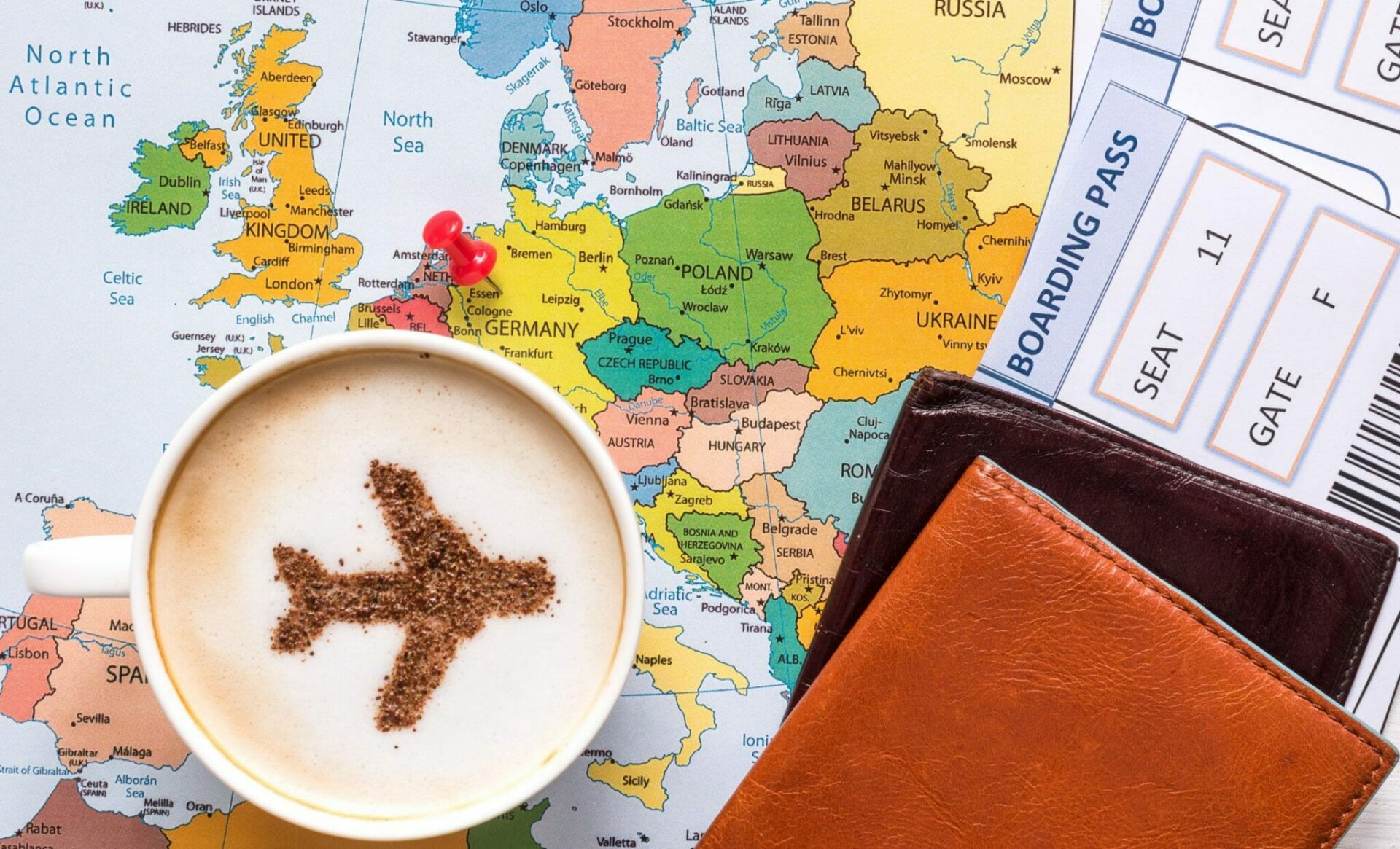 Urlaub buchen Reise buchen bei REISEBÜRO Wache Erfurt; Symbolbild: Landkarte auf einem Tisch, darauf Ausweise, Flugtickets und Cappuccino-Tasse mit weißem Schaum und darauf einem braunem Flugzeug