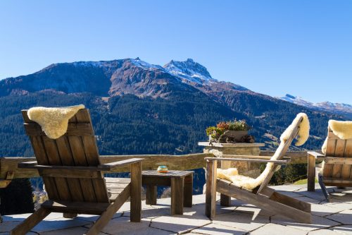 Erfurt REISEBÜRO Wache, Wellness-Hotel buchen, Hideaway buchen, Symbolbild: Holzstühle mit Fell darauf, im Hintergrund schroffe Berge mit letzten Schneeresten, die Sonne scheint