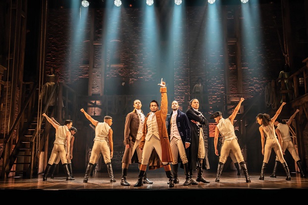 Musical Hamilton in Hamburg: Szenenbild, in dem Alexander Hamilton die Hand die Luft reckt, um ihn Tänzer, teils in Korsett und Unterhose, die ebenfalls ihre Hände in die Luft recken