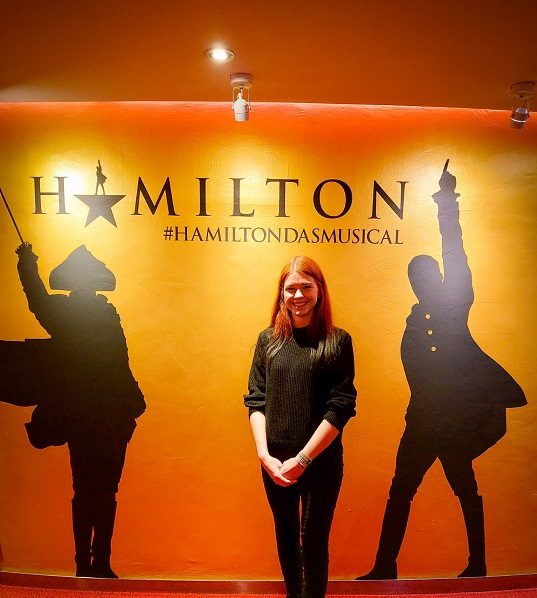 Das Musical "Hamilton" bei REISEBÜRO Wache Erfurt; Im Bild: Patricia Steinmann im Theater in Hamburg vor dem Schriftzug und den Schattenbildern von "Hamilton"