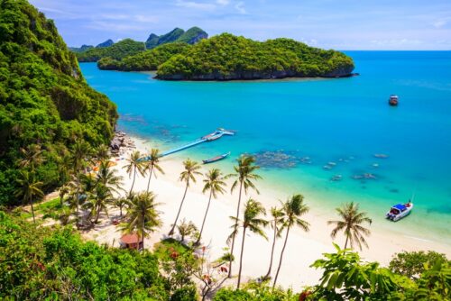 Blick auf den Marinepark auf Koh Samui in Thailand, Südostasien. REISEBÜRO Wache, Erfurt; zu sehen: grün bewachsene Inseln im türkisblauen Meer, im Vordergrund ein heller Strand, an dem hohe Palmen wachsen.