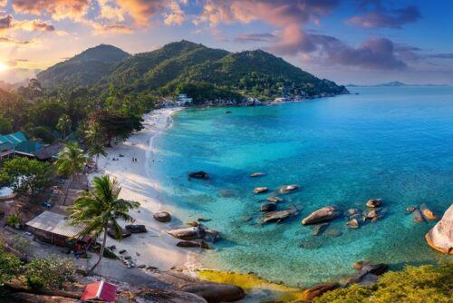 Thailand buchen bei REISEBÜRO Wache Erfurt; im Bild: tief stehende Sonne in einer Bucht auf Koh Samui in Thailand, Blick von oben: nah sinnd die sandige Bucht und türkisfarbenes Wasser, im Hintergrund sind grün bewachsene Berge und weitere Inseln