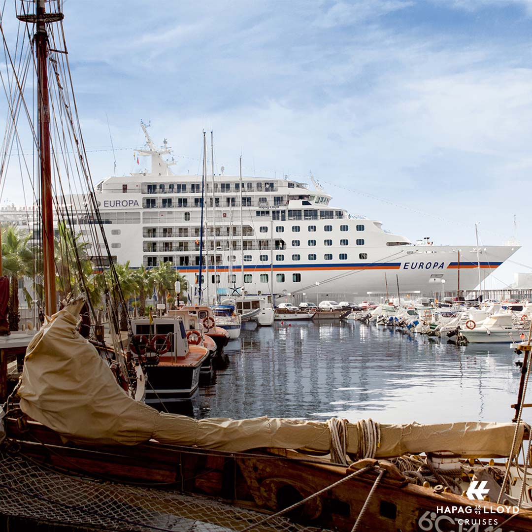 Kurzkreuzfahrt mit Stil von Hapag Lloyd Cruises, bei REISEBÜRO Wache Erfurt; im Bild: die große, weiße MS EUROPA fährt an malerischem Hafen mit schicken kleinen Segelbooten vorbei.