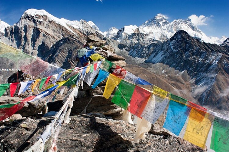 Reisen Bucket List: Trekking in Nepal beim REISEBÜRO Wache buchen; im Bild: Bunte Fähnchen im Himalaya in Nepal, im Hintergrund der schneebedeckte Mount Everest