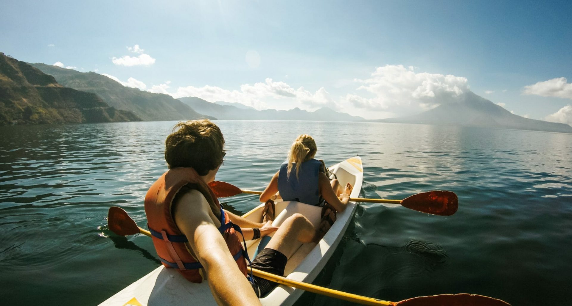 Symbolbild Urlaub Ausflüge buchen, im Foto: 2 Menschen fahren in einem Boot, im Hintergrund Berge