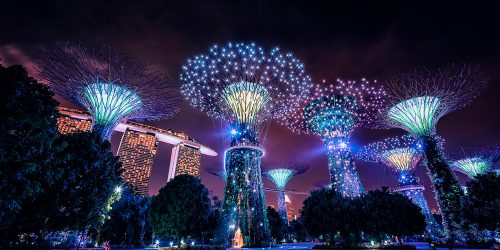 Weltreise Kreuzfahrt 2024/25 mit Nicko Cruises, buchbar bei REISEBÜRO Wache Erfurt; im Bild: erleuchtete Wolkenkratzer samt bunten Strahlen über ihnen Singapur bei Nacht