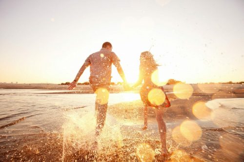 Symbolbild für Langzeiturlaub 2022/2023: Paar das durch Wasser rennt im goldenen Sonnenschein