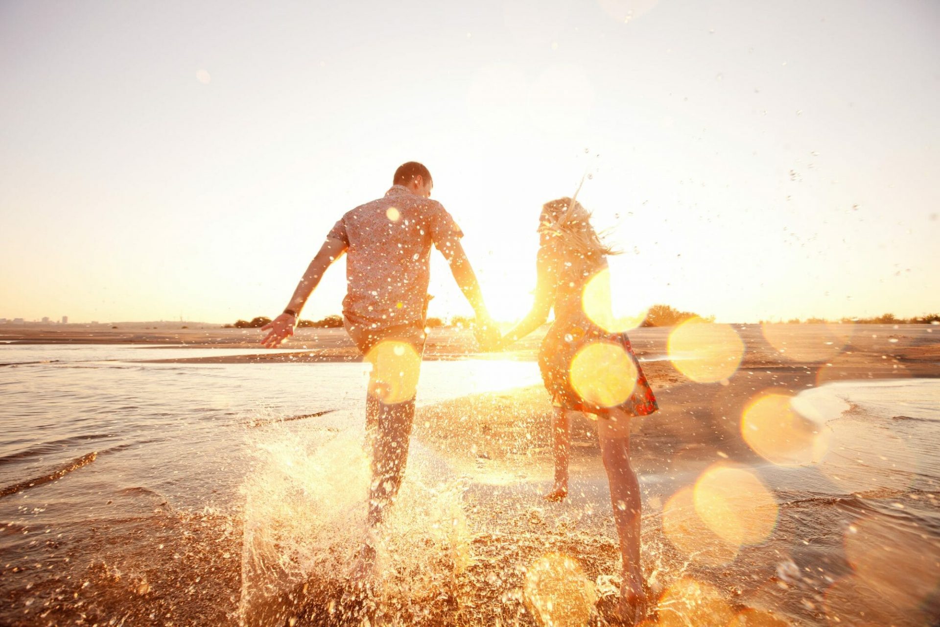 Symbolbild für Langzeiturlaub 2022/2023: Paar das durch Wasser rennt im goldenen Sonnenschein