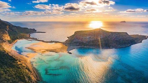 Kreta Urlaub Griechenland REISEBÜRO Wache Erfurt REISEBÜRO Wache Erfurt: Blick auf Balos Beach auf Kreta in Griechenland, Sonne versinkt hinter einem Fels im blau wirkenden Meer