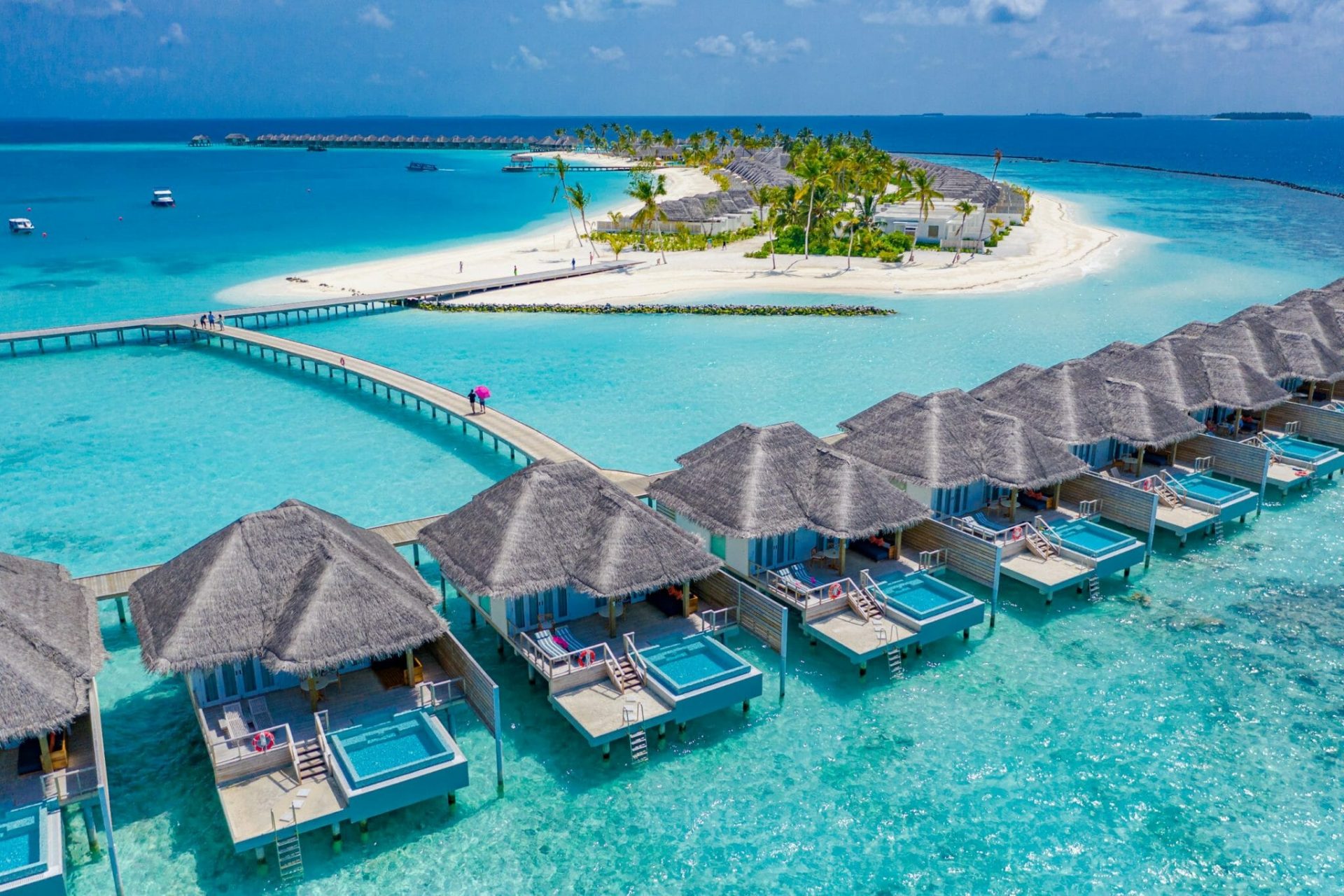 Wasservillen auf den Malediven, im Hintergrund sandfarbene Insel mit Palmen und türkisfarbenes Meer