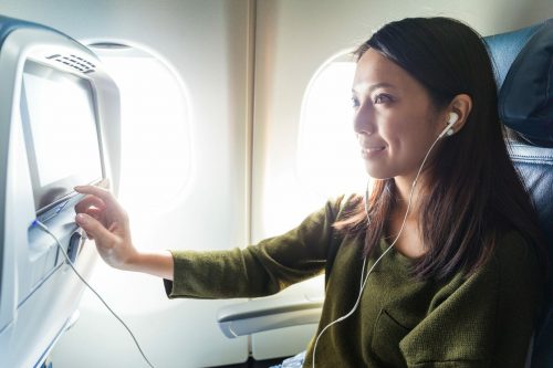 Erfurt REISEBÜRO Wache, Online-Check-In, Symbolbild zeigt: Frau mit Kopfhörern im Flugzeug vor einem Touchscreen