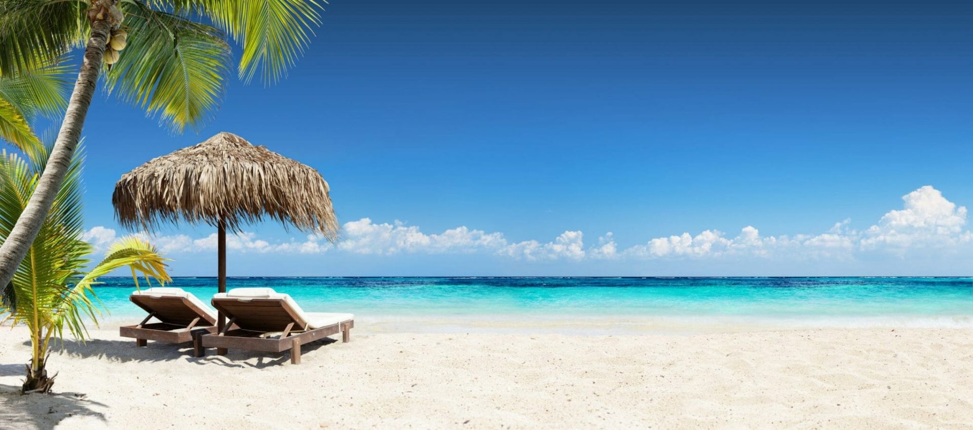 Symbolbild Reiseanfrage bei REISEBÜRO Wache stellen, zu sehen: weißer Sandstrand, türkisfarbenes Meer, Liegestühle unter Palmwedel gedecktem Sonnenschirm