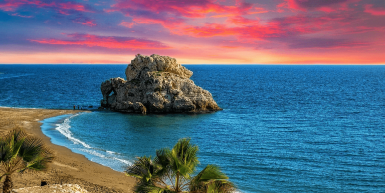 Spanien Urlaub buchen Erfurt bei REISEBÜRO Wache; im Bild: Blick auf Strand und Felsen im dunkelblauen Meer, von Málaga/Spanien aus, Sonnenuntergang strahlt Wolken dunkelrot an