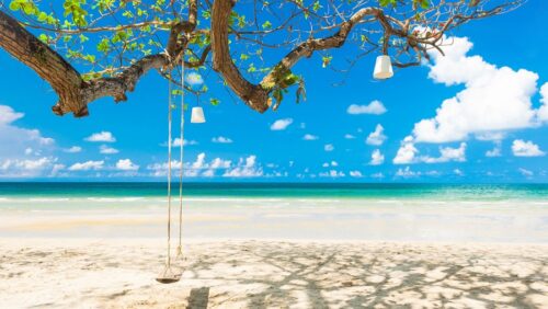 Thailand Urlaub buchen in Erfurt, Südostasien Urlaub; im Bild: Schaukel an einem Ast am Strand, grüne Blätter hängen am Baum, im Hintergrund das türkisfarbene Meer und blauer Himmel mit weißen Wölkchen
