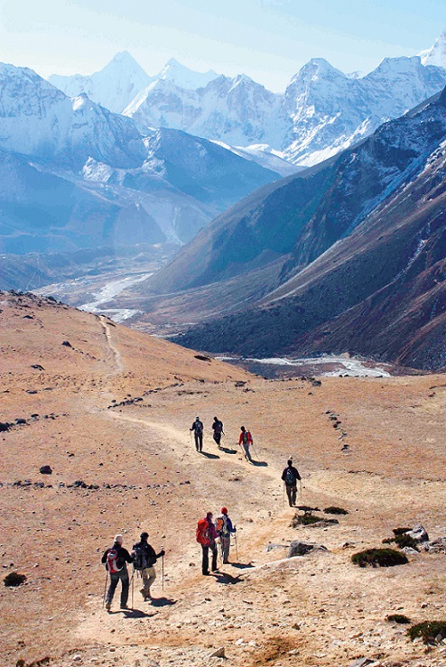 Trekking in Nepal mit kleiner Gruppe, Bucket List Reise vom REISEBÜRO Wache Erfurt; im Bild: Menschen in Wanderausrüstung entlang einem kargen Pfad, im Hintergrund teils schneebedeckte Berge bei Lombuche