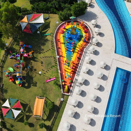 Urlaub Türkei 5 Sterne Hotel Kinder bei REISEBÜRO Wache Erfurt buchen: Bild von oben auf die bunt gestaltete Kinder-Pool-Anlage mit mehreren Rutschen, daneben Sonnenschirme, daneben ein länglicher blauer Pool