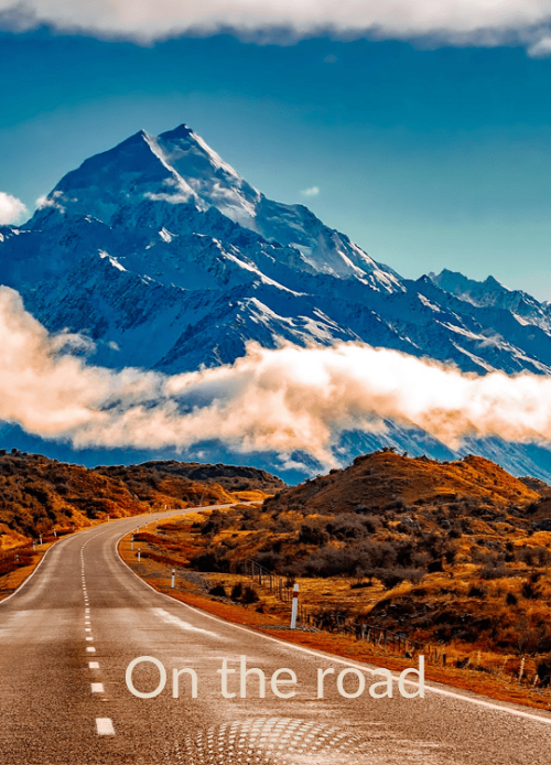 Urlaub Neuseeland buchen bei REISEBÜRO Wache Erfurt; im Bild: blau erscheinende Berge mit tief hängenden Wolken davor; eine Straße führt hin, sie und die Umgebung wirken rötlich